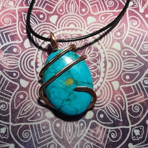 May include: A turquoise gemstone pendant wrapped in copper wire, hanging from a black cord. The pendant is a natural stone with a green and blue color variation.