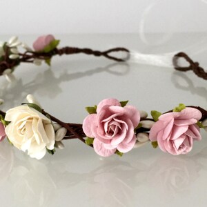 May include: A floral crown with pink and white paper roses and small white flowers on a brown vine base.