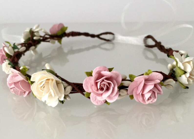 May include: A floral crown with pink and white paper roses and small white flowers on a brown vine base.