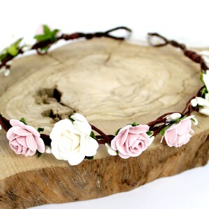 May include: A brown floral crown with pink and white roses and green leaves.