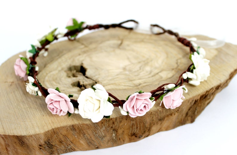 May include: A brown floral crown with pink and white roses and green leaves.