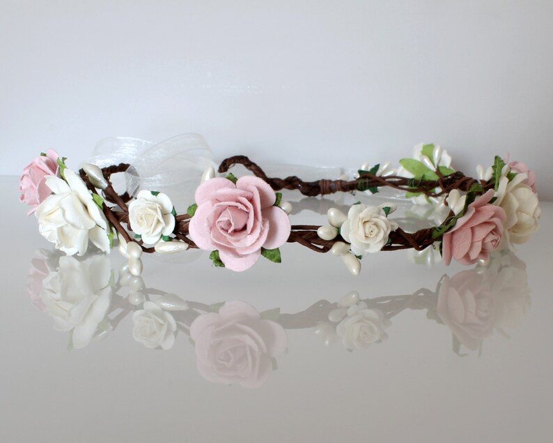 May include: A delicate floral crown with pink and white roses, pearl accents, and brown vines.
