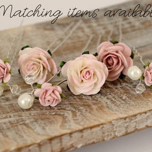May include: Six pink and white paper flower hair pins with pearl accents. The pins are arranged on a wooden surface.