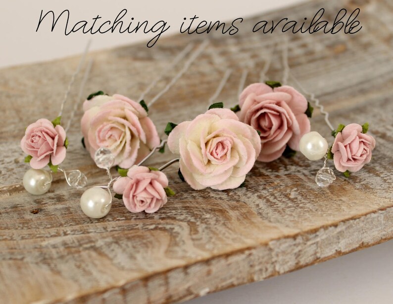 May include: Six pink and white paper flower hair pins with pearl accents. The pins are arranged on a wooden surface.