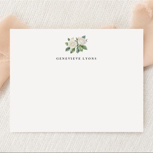 May include: White card with a floral design in the top right corner. The text "GENEVIEVE LYONS" is centered below the floral design.