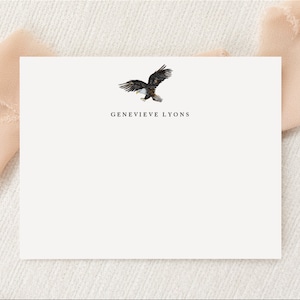 May include: A white card with a black and brown eagle illustration and the text "GENEVIEVE LYONS" printed in black.