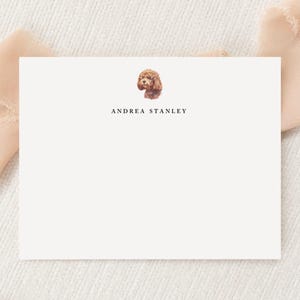 May include: A rectangular white stationery card featuring a small watercolor illustration of a brown curly-haired dog at the top center. Below the dog illustration, the name ANDREA STANLEY is printed in a simple, black, uppercase serif font.