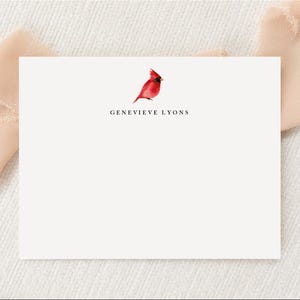 May include: A white card with a red cardinal illustration and the text "Genevieve Lyons" printed in black.