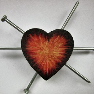 May include: A heart-shaped object with a textured surface, featuring a gradient of colors from black to red and gold. Six silver nails are positioned around the heart, creating a visual contrast.