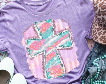 May include: Purple t-shirt with a floral cross design. The cross is green, pink, and white with a glittery effect. The background is a pink and white striped pattern.