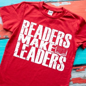 May include: Red t-shirt with white text that reads "Readers Make Leaders" and a white graphic of an open book.