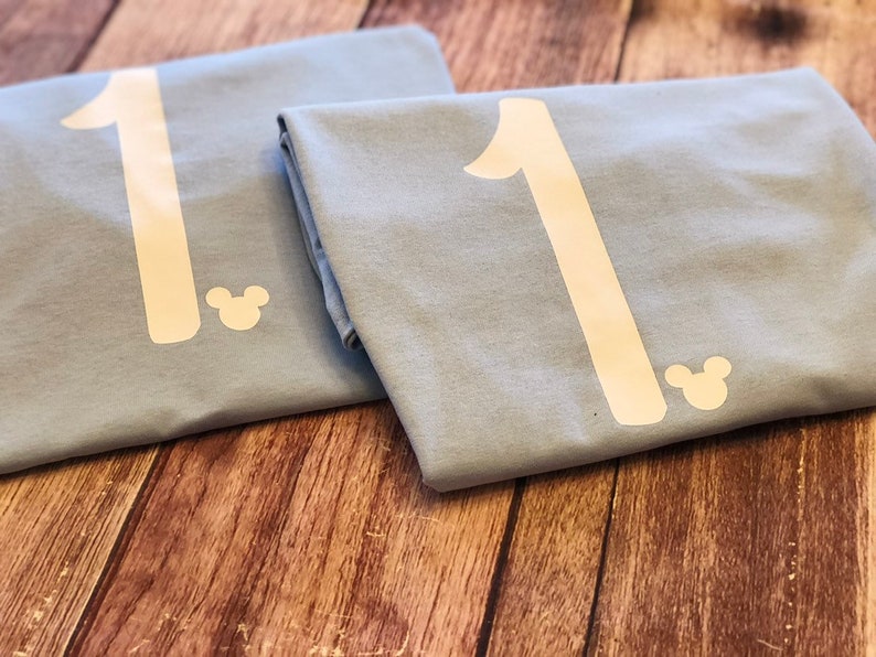 May include: Two light blue t-shirts with a white number "1" and a white Mickey Mouse silhouette on each.