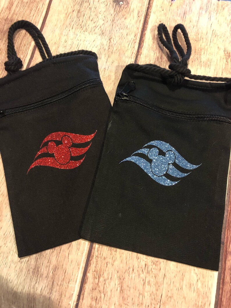 May include: Two black drawstring bags with a zipper closure. Each bag features a Disney Cruise Line logo with a Mickey Mouse head in the center. One bag has a red glitter logo and the other has a blue glitter logo.