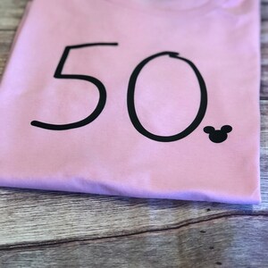 May include: A pink t-shirt with the number 50 printed in black and a small black Mickey Mouse silhouette.