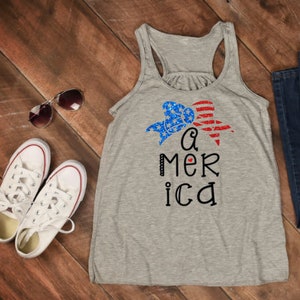K&ouml;nnte beinhalten: Ein graues Tanktop mit einer rot-wei&szlig;-blauen Schleife und dem Text "a mer ica" mit einem kleinen roten Herzen in der Mitte des Wortes "america".