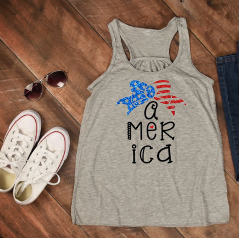 K&ouml;nnte beinhalten: Ein graues Tanktop mit einer rot-wei&szlig;-blauen Schleife und dem Text "a mer ica" mit einem kleinen roten Herzen in der Mitte des Wortes "america".