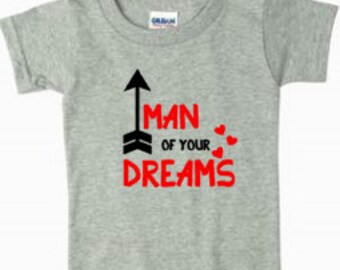 Puede incluir: Camiseta gris de manga corta con texto negro que dice "Man of your Dreams" con una flecha apuntando hacia arriba y corazones rojos.