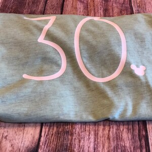 May include: A light green t-shirt with the number 30 printed in white on the front. A small white Mickey Mouse head is printed to the right of the number.