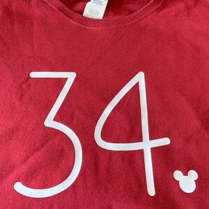 May include: A maroon t-shirt with the number 34 printed in white. A white Mickey Mouse silhouette is in the bottom right corner.
