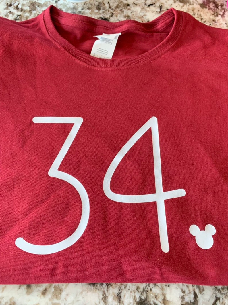 May include: A maroon t-shirt with the number 34 printed in white. A white Mickey Mouse silhouette is in the bottom right corner.