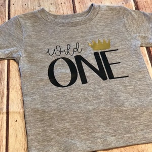 May include: Gray short-sleeved t-shirt with the text "wild one" in black lettering and a gold crown above the word "one".