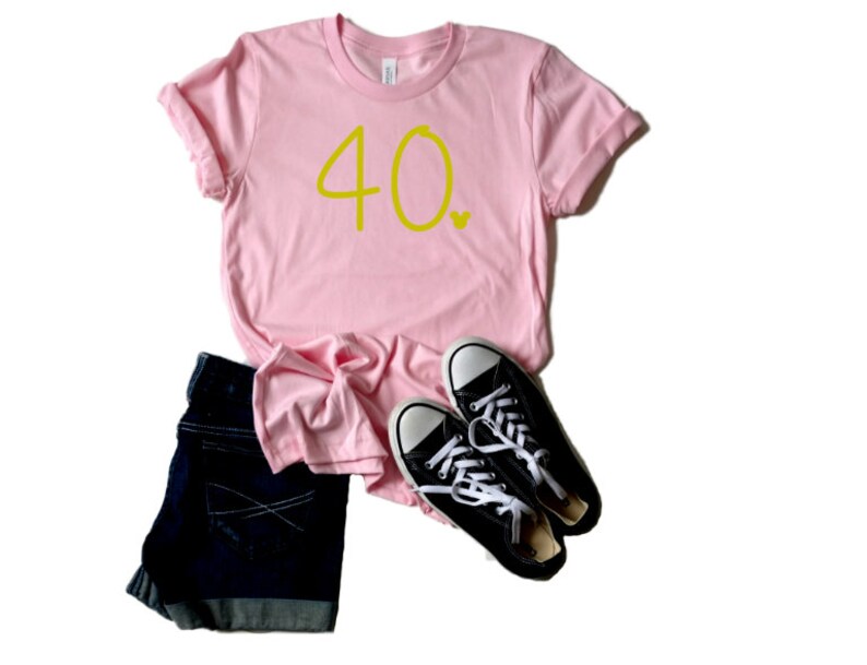 May include: A pink t-shirt with the number 40 in yellow lettering. The shirt is folded and laid flat on a white background with a pair of black sneakers.