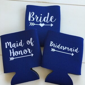 Pode incluir: Tr&ecirc;s coolers de lata azuis com texto branco e flechas. Os coolers dizem "Bride", "Maid of Honor" e "Bridesmaid".