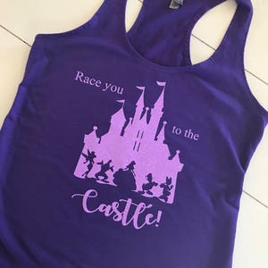 May include: Purple tank top with a pink silhouette of Cinderella's castle and characters. The text "Race you to the castle!" is printed on the shirt.