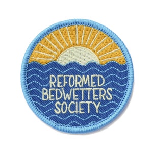 May include: A blue and yellow embroidered patch with a sun setting over the ocean and the text "REFORMED BEDWETTER SOCIETY".
