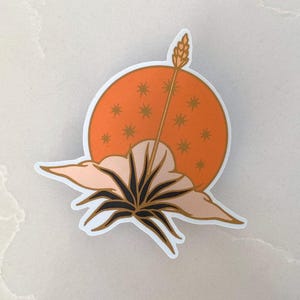 May include: A sticker featuring a stylized illustration of a plant with a single stalk rising from the center, set against a background of an orange sun with gold stars. The plant is depicted with a dark green stem and leaves, and the sun has a soft, peachy orange hue.