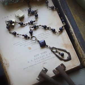 May include: A dark blue and gold necklace with a star-shaped pendant hangs on an old book. The book is open to a page with the text "THE PRINCIPLES OF SCIENCE" and "NEW YORK: A.S. BARNES & BURT 11 & 13 JOHN STREET 1860".