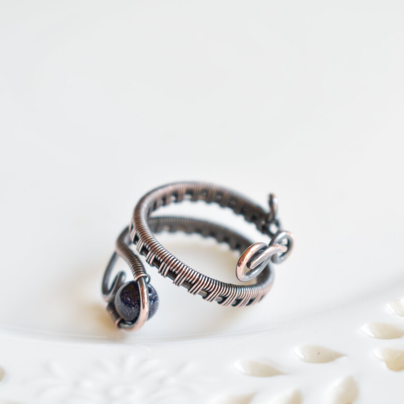 May include: A copper wire ring featuring a dark blue stone. The ring is crafted from two intertwined wires, one of which is wrapped around the stone.