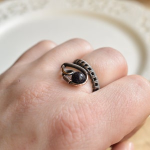 May include: A copper wire ring featuring a black gemstone. The ring is wrapped around the finger and has a distinctive design.