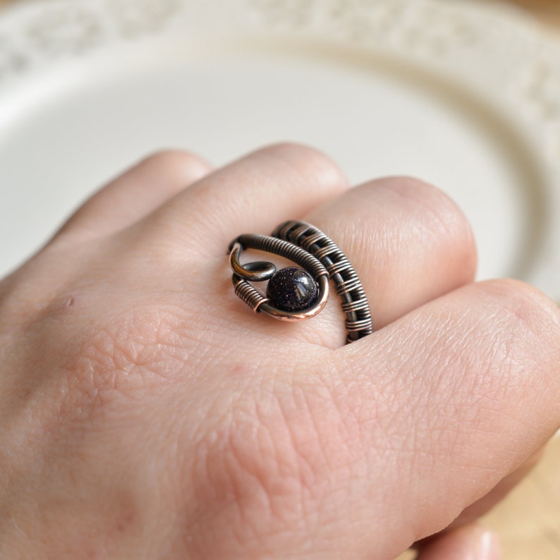 May include: A copper wire ring featuring a black gemstone. The ring is wrapped around the finger and has a distinctive design.