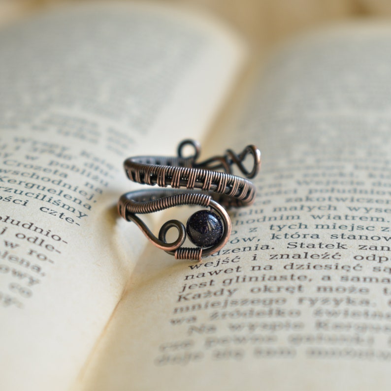 May include: A copper wire ring featuring a dark blue gemstone. The ring is handcrafted and has a distinctive, organic design.
