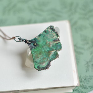 May include: A green and copper ginkgo leaf pendant necklace with a delicate chain. The pendant is made of metal and has a textured surface.