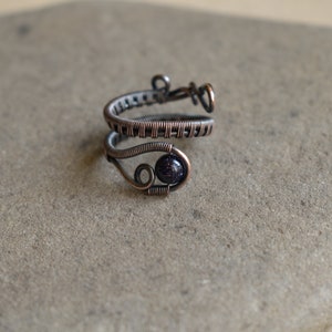 May include: A copper wire ring featuring a dark blue gemstone. The ring is wrapped in a woven pattern and has a delicate design.