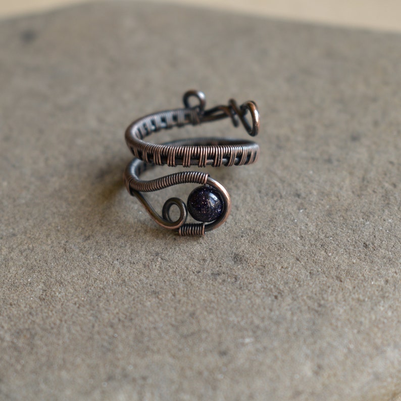 May include: A copper wire ring featuring a dark blue gemstone. The ring is wrapped in a woven pattern and has a delicate design.