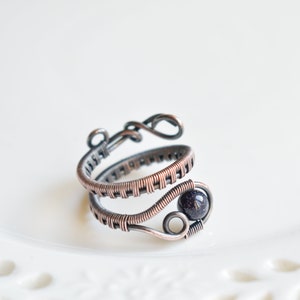 May include: A copper wire ring featuring a dark blue gemstone. The ring is crafted from multiple strands of wire that are interwoven.