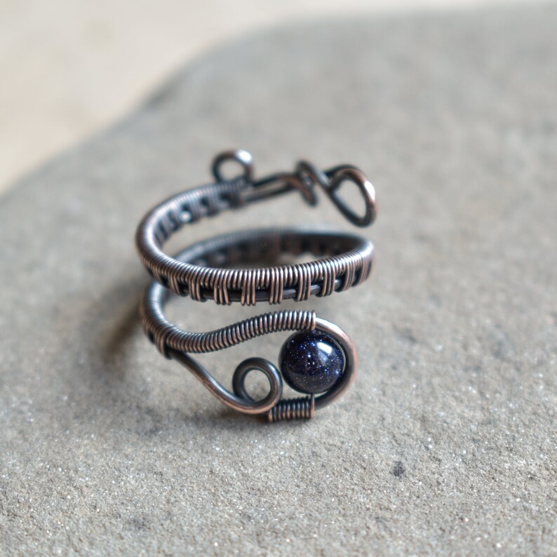 May include: A silver wire wrapped ring featuring a dark blue gemstone. The ring is crafted from multiple strands of wire that are woven together.