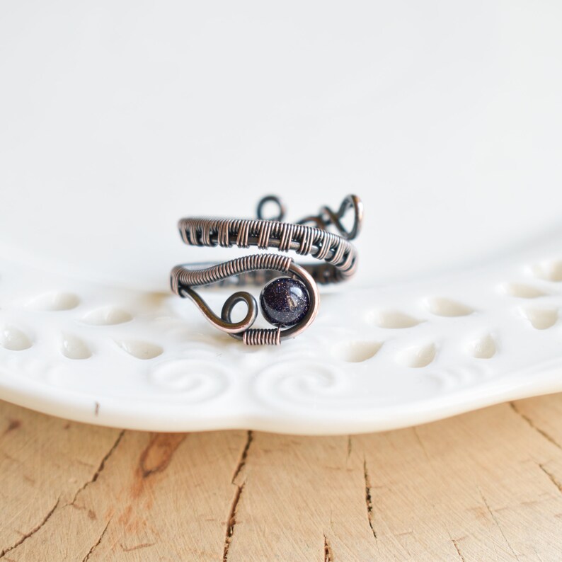 May include: A copper wire ring featuring a dark purple gemstone. The ring is crafted with a woven wire design.