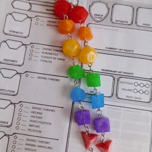 May include: A rainbow-colored eyeglass chain featuring a variety of geometric beads. The chain includes red, orange, yellow, green, blue, and purple beads, connected by silver-colored chains. The chain is designed to hold eyeglasses.