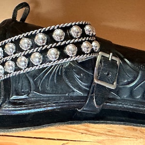 May include: A black leather holster with a silver buckle and a silver beaded strap. The strap has two rows of round beads.