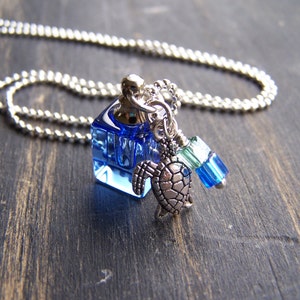 Könnte beinhalten: Eine silberne Kettenkette mit einem blauen Glasflaschen-Anhänger, einem silbernen Schildkröten-Anhänger und blauen und grünen Glasperlen.