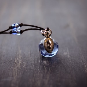 May include: A brown cord necklace with blue glass beads and a silver charm shaped like a football.