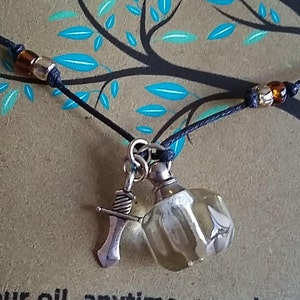 May include: A black cord necklace with a small, clear glass bottle pendant and a silver sword charm. The bottle has a faceted design and is filled with a clear liquid.