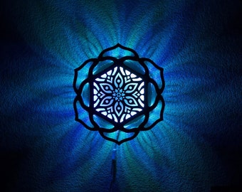 May include: A decorative wall light with a floral design. The light is black with a white and blue illuminated center, casting a blue glow on the wall. The light fixture is shaped like a flower.