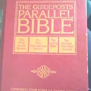 May include: A red book titled "The Guideposts Parallel Bible" with gold lettering. The book compares four popular Bible translations in parallel columns. The cover includes the King James Version, New International Version, The Living Bible, and Revised Standard Version.