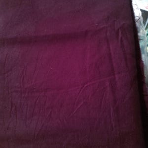 May include: A piece of deep purple fabric with visible folds and a soft texture. The fabric appears to be a solid color, with subtle variations in tone across its surface. The edges of the fabric are slightly frayed.