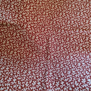 May include: Close-up of a fabric with a repeating pattern of white leaves on a deep red background. The leaves are detailed and create a textured appearance. The fabric is likely used for clothing or home decor.